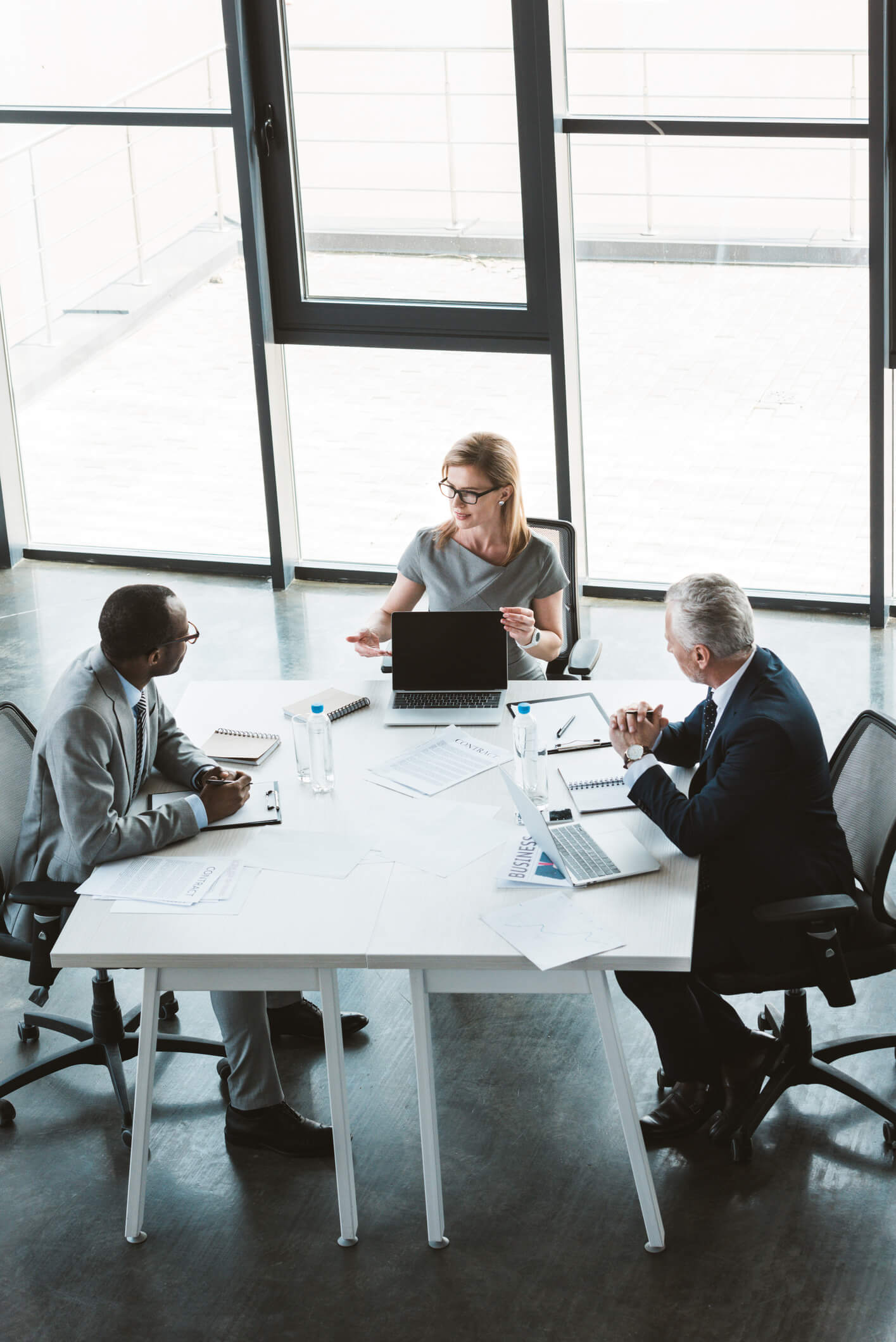 Vue d’angle élevé de femme d’affaires montrant ordinateur portable avec écran blanc et en regardant des hommes d’affaires multiethniques au cours de la réunion 